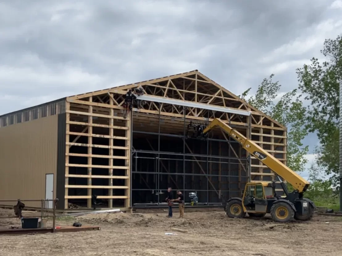 Men and equipment installing a bifold door on a post frame building.