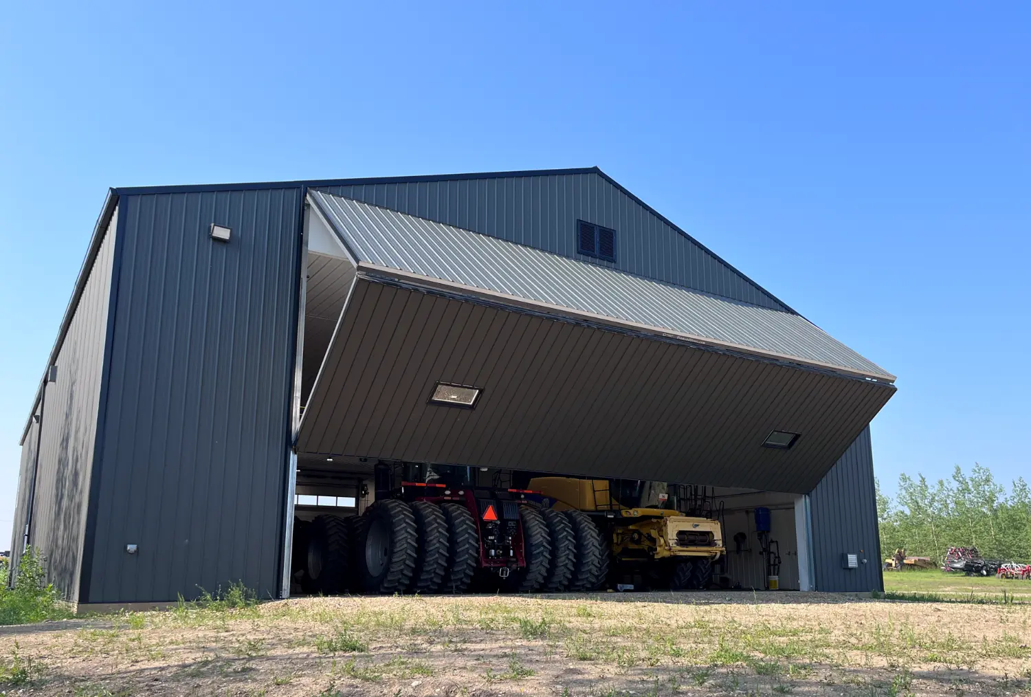 A partially opened, large bifold door on a brown shop with a red tractor and yellow combine inside.