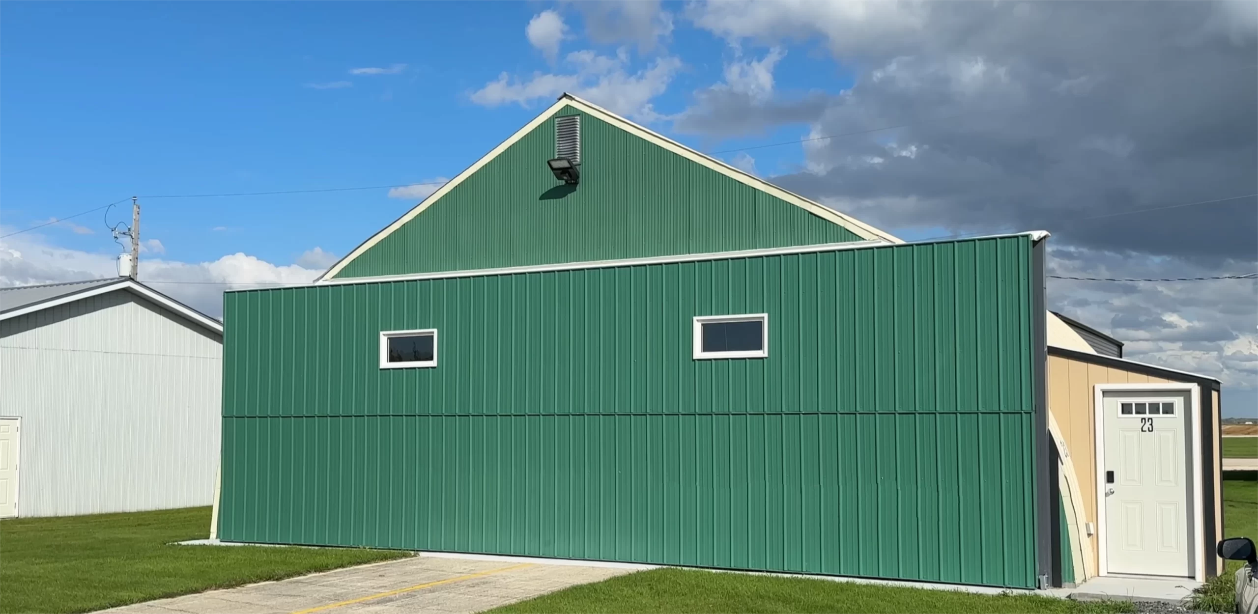 A green quonset hangar with a bifold door. The bifold door has two windows.